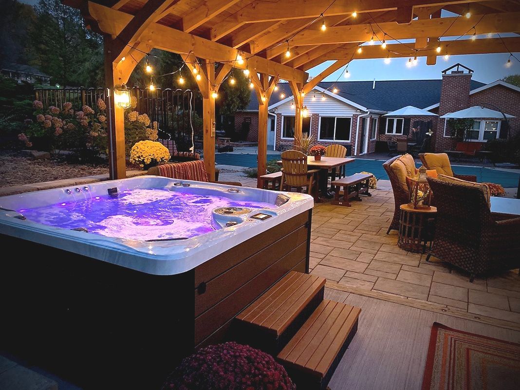 Backyard hot tub under a pergola with string lights at dusk