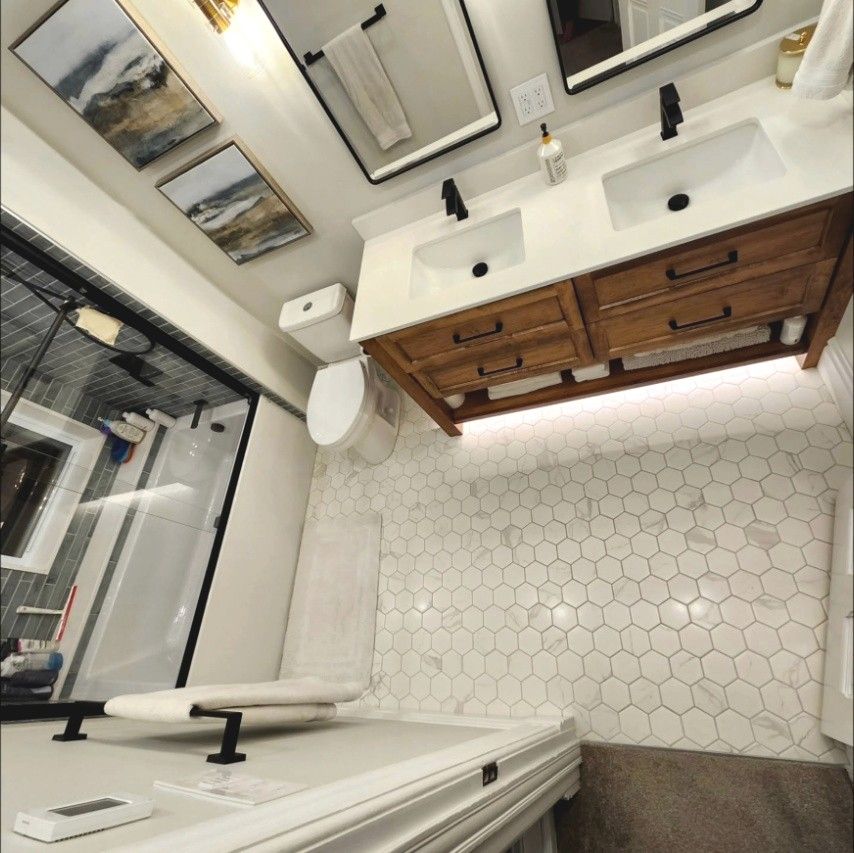Renovated bathroom with a lit double vanity, hex tile floor and glass shower