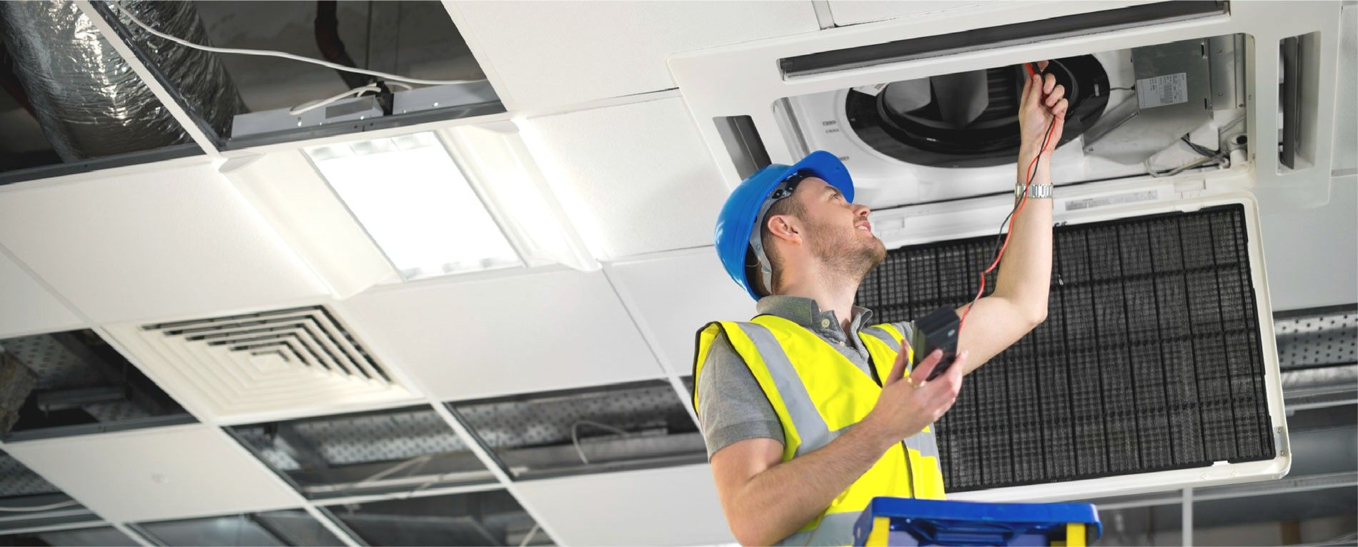 Electrician working on ceiling fixtures in a commercial space