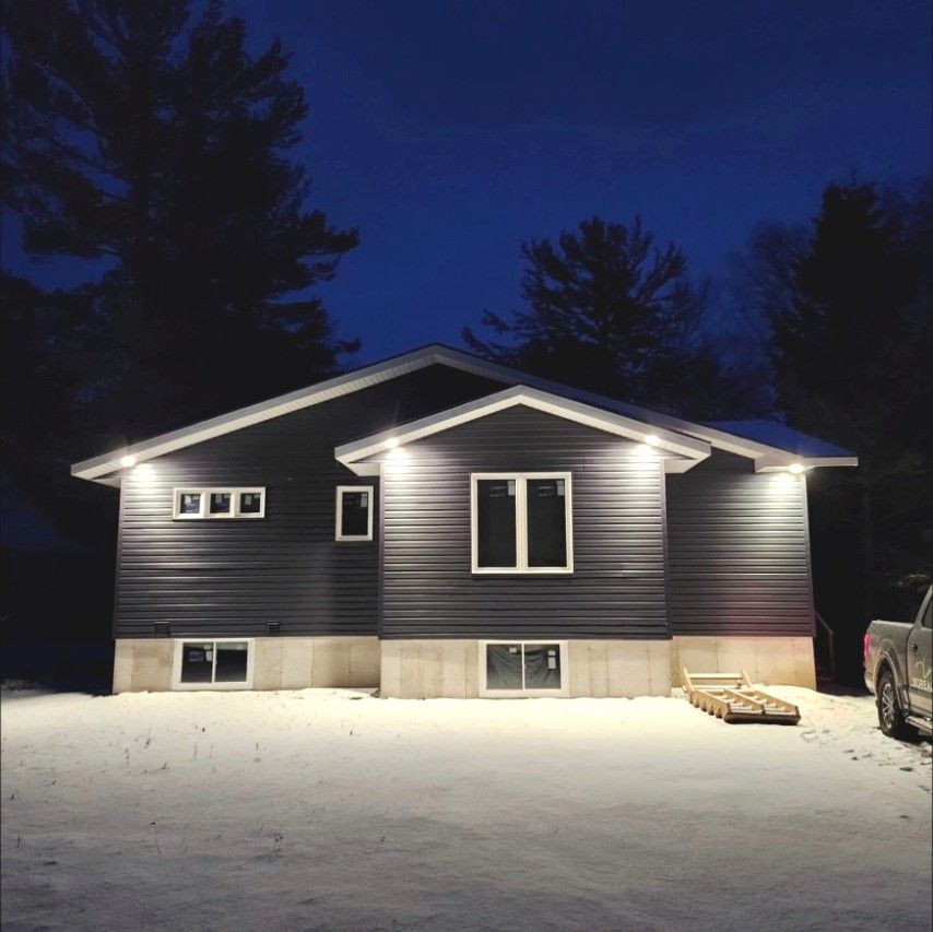 New home at night with soffit pot lights glowing over the siding and snow