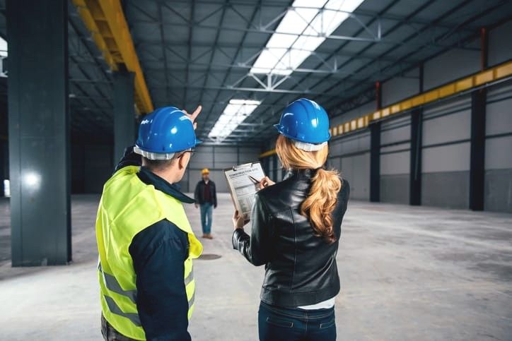 Two people in hard hats reviewing a checklist inside a large building